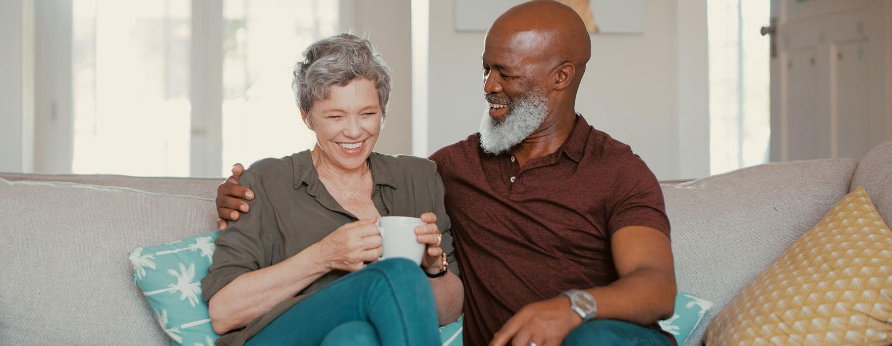 Settle into comfort at Serenity Towers at Brockton smiling, older couple, sit together on a couch